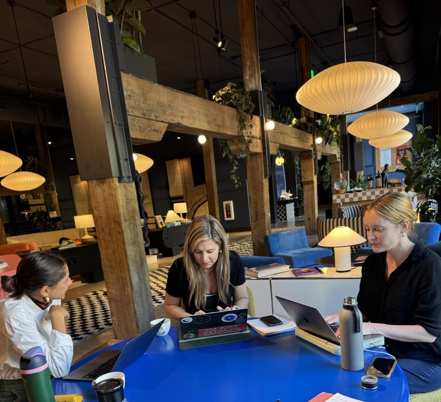Three colleagues working around a blue table, laptops and notebooks open