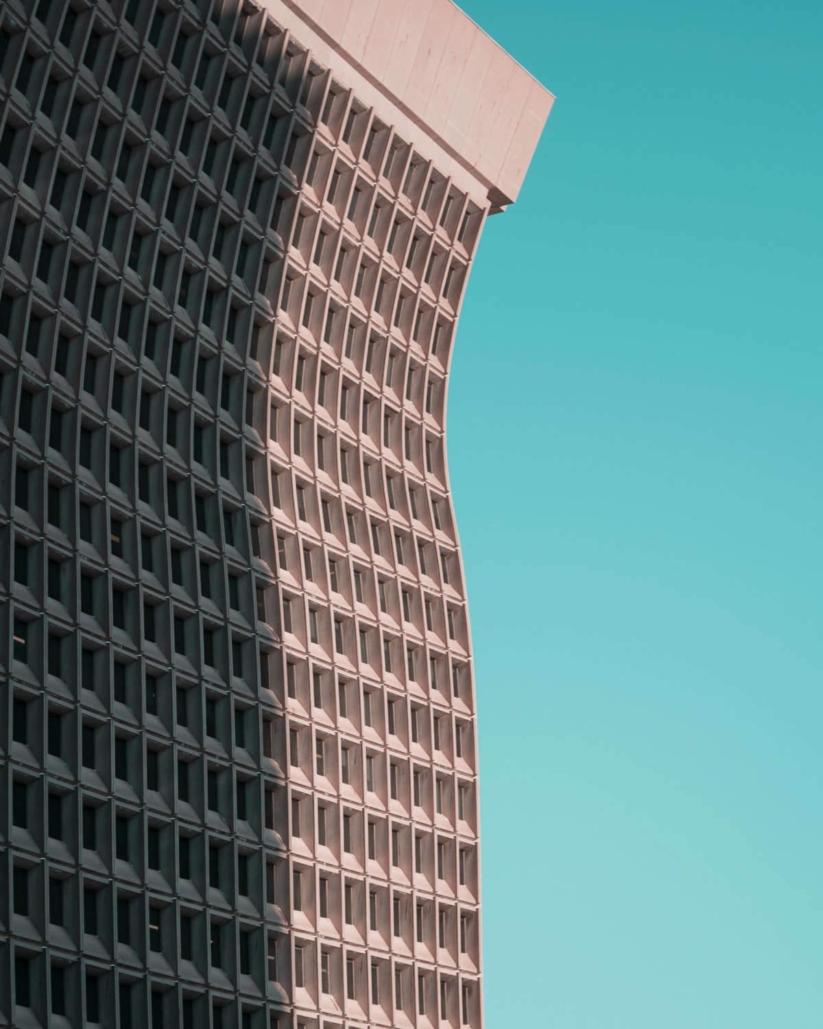 A curved modernist high-rise against a clear teal sky